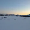 Gruppo di ciaspolatori in fila indiana al tramonto con la guida e la lanterna: ciaspolata notturna