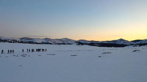 Gruppo di ciaspolatori in fila indiana al tramonto con la guida e la lanterna: ciaspolata notturna