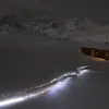 Escursionista con la frontale in marcia di sera verso un rifugio illuminato, sul passo del Sempione in inverno