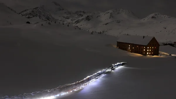 Escursionista con la frontale in marcia di sera verso un rifugio illuminato, sul passo del Sempione in inverno
