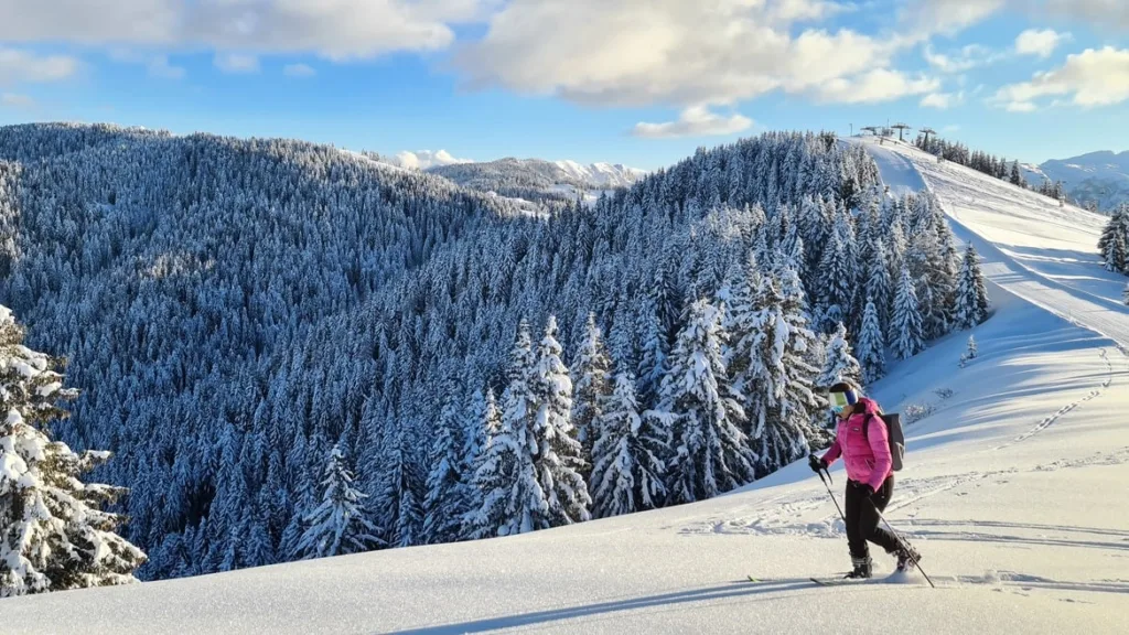 Neve scialpinismo: scialpinista con giacca rosa risale con le pelli un pendio innevato