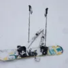 Snowboard con attacchi appoggiato sulla neve accanto a bastoncini e sci