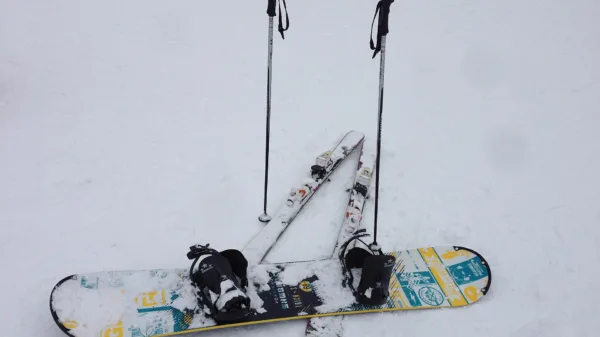 Snowboard con attacchi appoggiato sulla neve accanto a bastoncini e sci