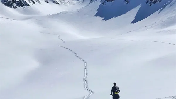 Scialpinista in salita lungo una traccia in un ampio vallone innevato