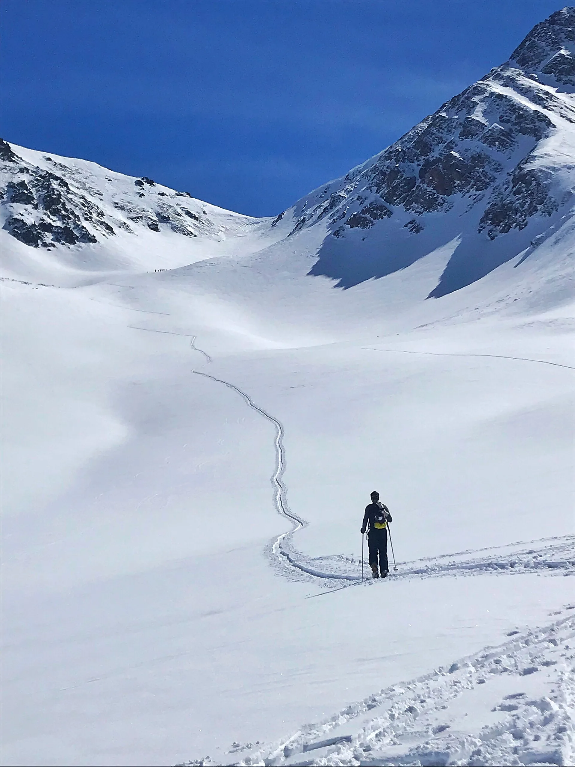Scialpinista in salita lungo una traccia in un ampio vallone innevato